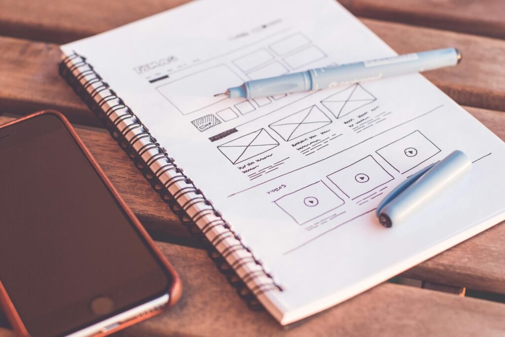 Planejamento de site em caderno com wireframe, celular e caneta representando desenvolvimento web